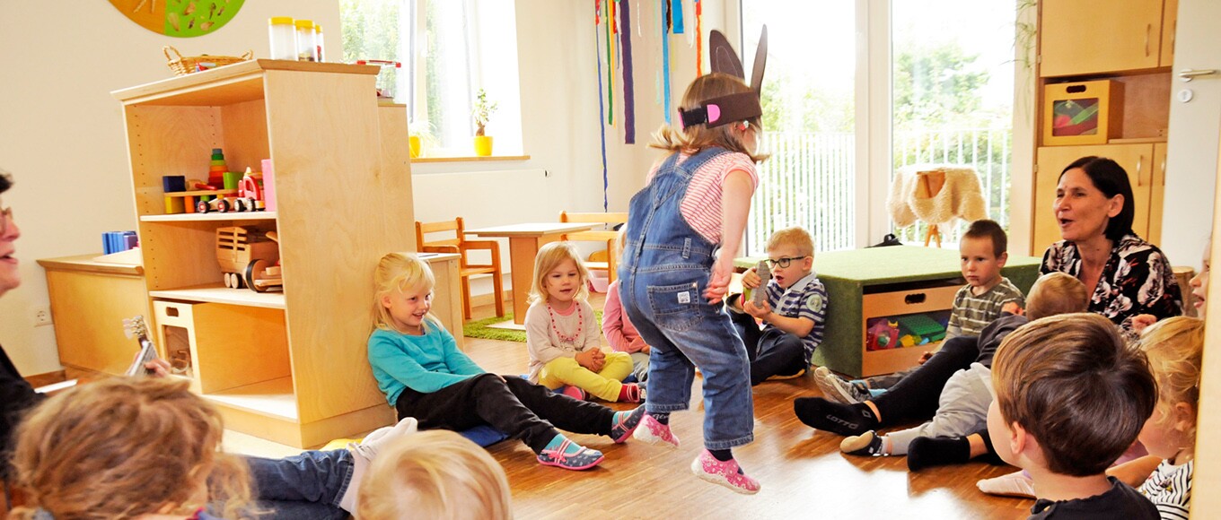 Eine Gruppe aus Kindern und Betreuerinnen schaut dem Auftritt eines kleinen Mädchens mit Hasenohren zu