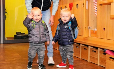 Zwei Kleinkinder in Jacken winken in die Kamera
