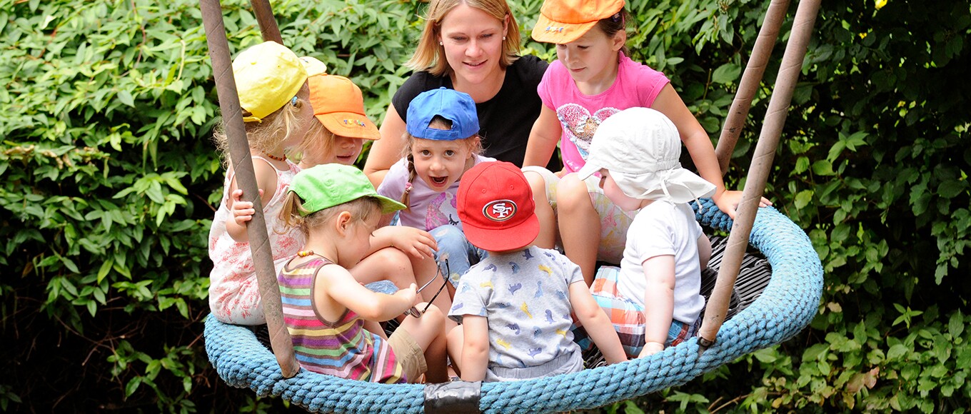 Kleine Kinder auf einer Netzschaukel und ihre Betreuerin